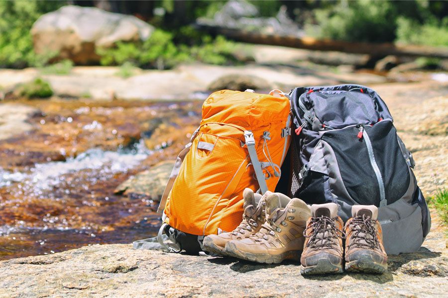 Hiking gear banner background in summer forest two backpacks and trek shoes boots for hikers couple camping travel outdoor adventure panoramic header.